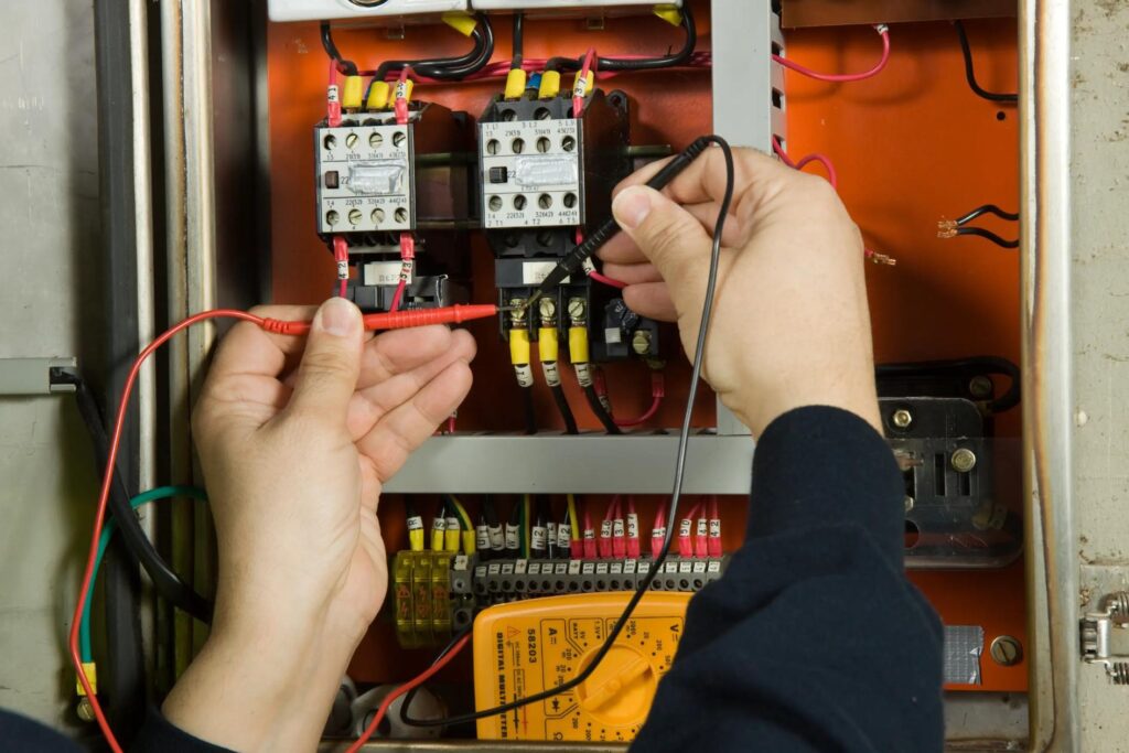 An electrician using soldering tools inside a bank of wiring