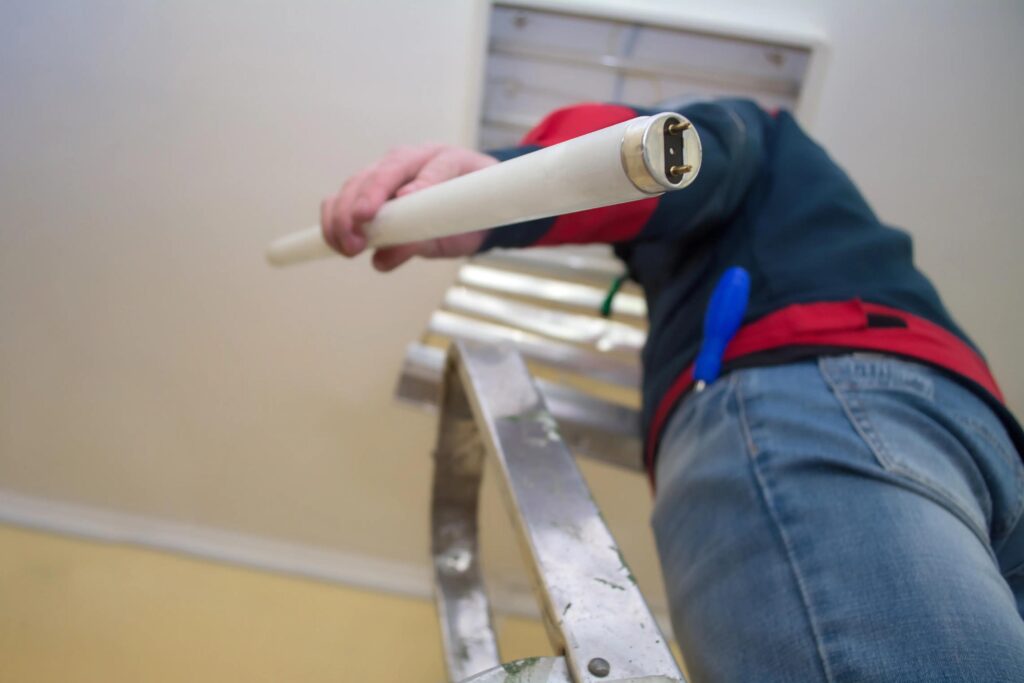 An electrician on a ladder installing a florescent light
